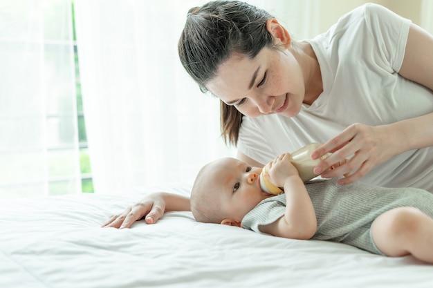 Bebe leche de una botella con la madre junto a él