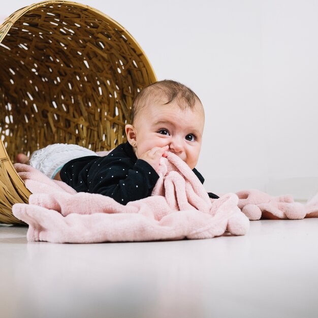 Bebé lindo en la cesta que mastica la manta