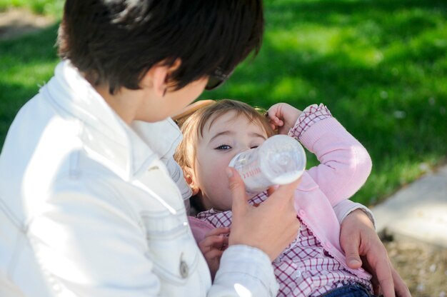 Bebé niña bebiendo leche de la botella de bebé. Madre alimentando a hija de la botella.
