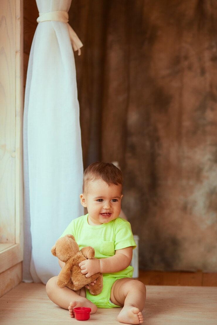 Foto gratuito el bebé pequeño guarda un juguete y se sienta junto a la ventana