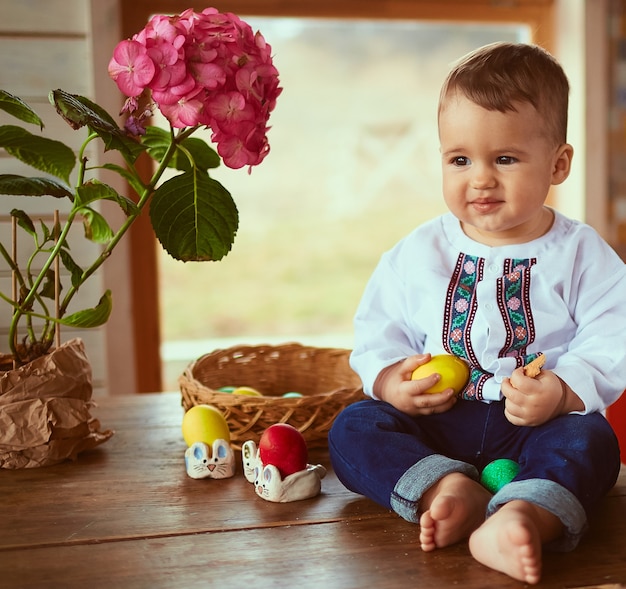 El bebé pequeño tiene un huevo amarillo y se sienta en la mesa