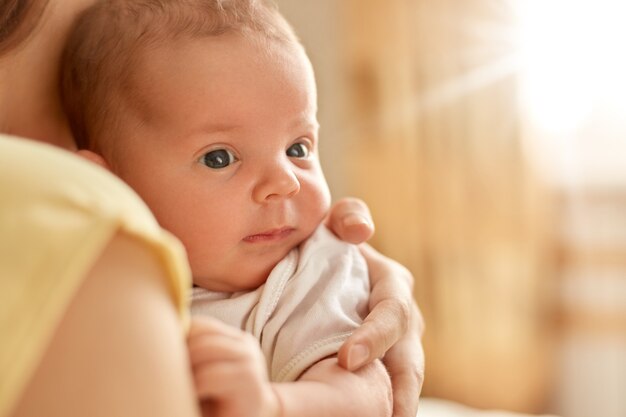 Bebé recién nacido en los brazos de su madre, mirando hacia otro lado y estudiando cosas externas, mamá sin rostro con niño interior, lindo bebé con mamá.