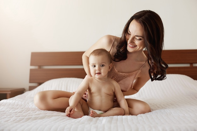 Bebé recién nacido sentado en casa con su madre jugando y sonriendo. Mamá disfrutando de su maternidad.