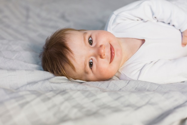 Bebé rubio adorable sobre cama blanca