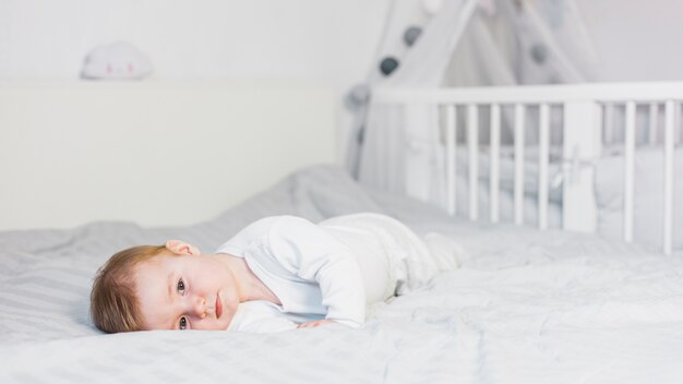 Bebé rubio adorable tumbado sobre cama blanca