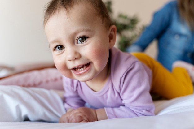 Bebé sonriente acostado en la cama mientras su madre está sentada a su lado