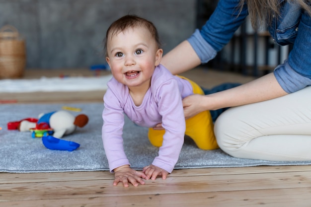 Bebé sonriente gateando y retenido por su madre