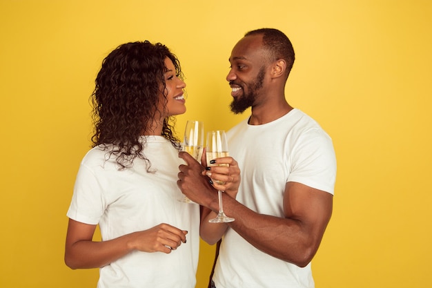 Beber champán. Celebración del día de San Valentín, feliz pareja afroamericana aislada sobre fondo amarillo de estudio. Concepto de emociones humanas, expresión facial, amor, relaciones, vacaciones románticas.