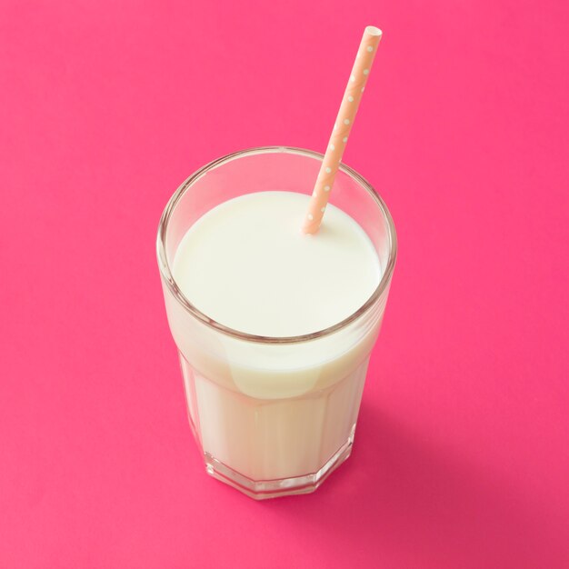 Beber paja en el vaso de leche sobre el fondo rosa