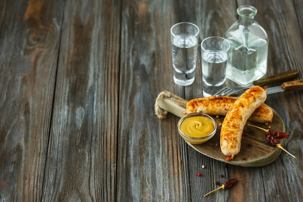 Foto gratuita bebida alcohólica con salchichas fritas y salsa sobre fondo de madera. bebida artesanal pura de alcohol y merienda tradicional. espacio negativo. celebrando la comida y deliciosa.