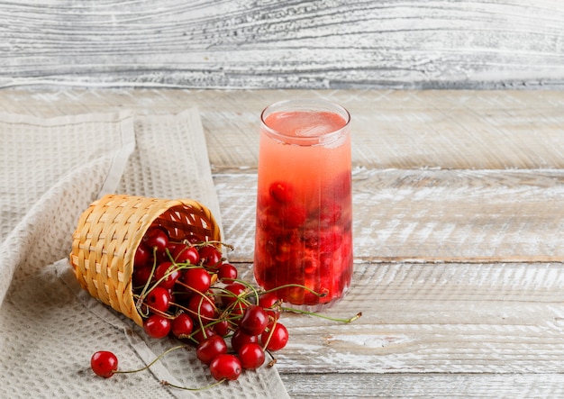 Bebida de cereza en una jarra con cerezas vista de ángulo alto en madera y papel de cocina