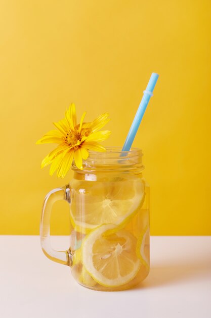 Bebida fresca con limón, vidrio decorado con flor amarilla.