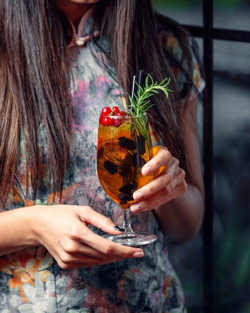 Bebida fría en un vaso con bayas en manos de una niña