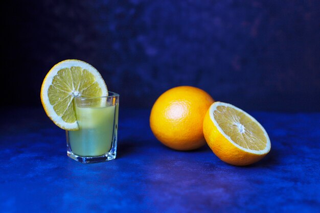 Bebida de naranja alcohólica en vaso de chupito con rodaja de naranja y naranja sobre fondo oscuro