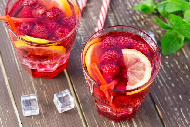 Bebida de verano con frambuesas, limón y hielo en una mesa de madera antigua