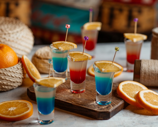 Bebidas alcohólicas azules y rojas con rodajas de naranja.