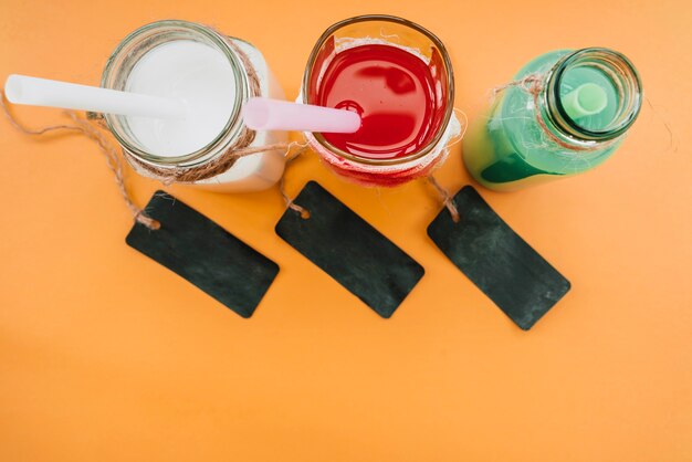 Bebidas en botellas de vidrio con popotes junto a etiquetas oscuras