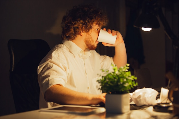 Bebiendo café. Hombre que trabaja en la oficina, quedándose hasta tarde en la noche.