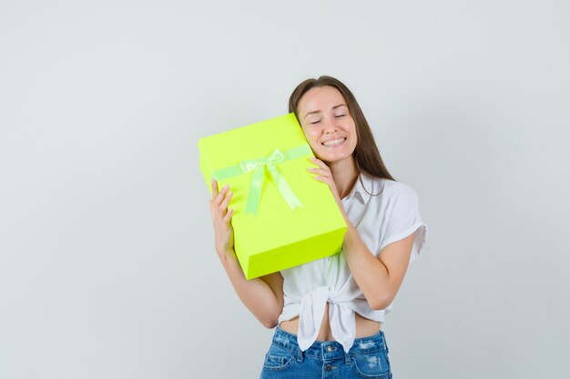 Bella dama abrazando la caja de regalo en blusa blanca, jeans y mirando amado, vista frontal.