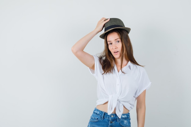 Bella dama con blusa blanca, sombrero quitándose el sombrero y mirando enfocado.