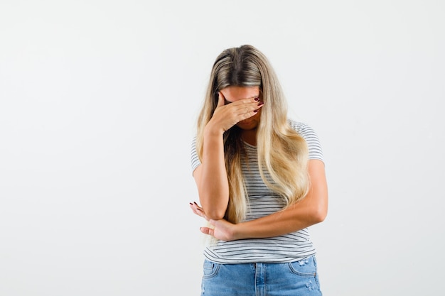 Foto gratuita bella dama en camiseta sosteniendo la mano en el ojo y mirando ofendido, vista frontal.