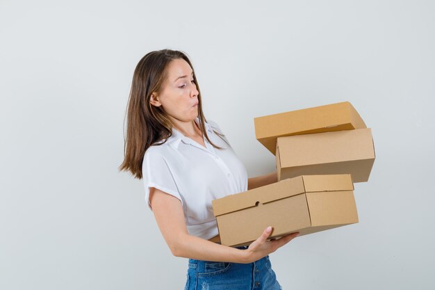 Bella dama llevando cajas en blusa blanca y mirando preocupado, vista frontal.