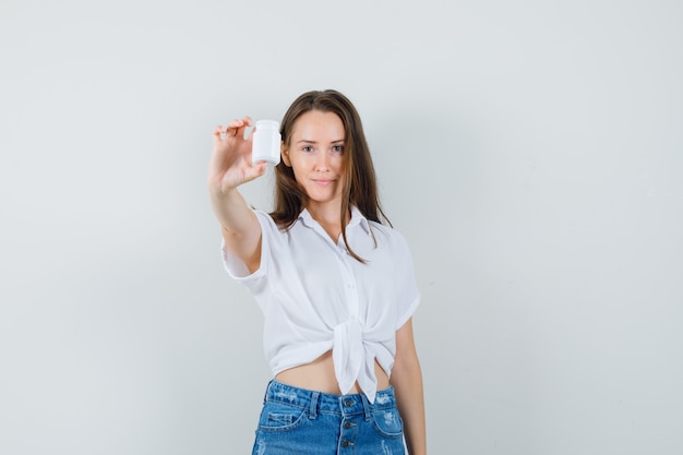 Bella dama mostrando botella de píldoras en blusa blanca, vista frontal.