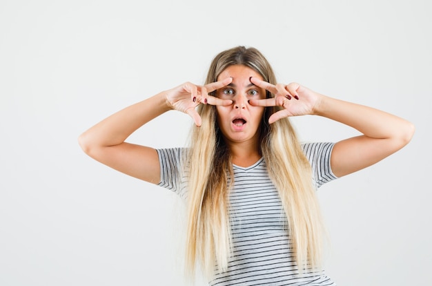 Foto gratuita bella dama mostrando el signo v sobre los ojos en camiseta y luciendo extraña, vista frontal.