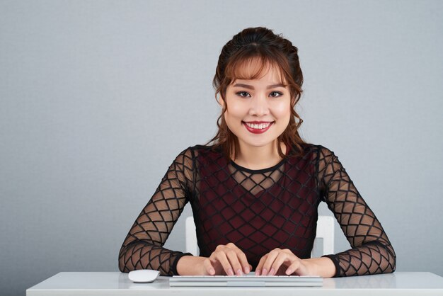 Bella dama de negocios sonriendo a la cámara con los brazos en el teclado de la computadora