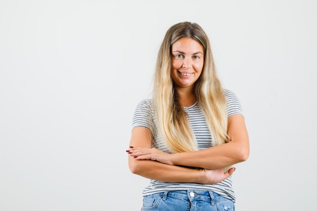 Bella dama de pie con los brazos cruzados en camiseta y luciendo fresca. vista frontal.