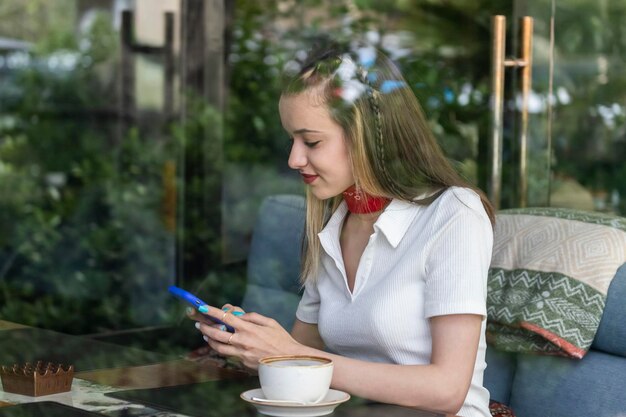 Bella dama sonriente sentada en el restaurante y jugando con su teléfono