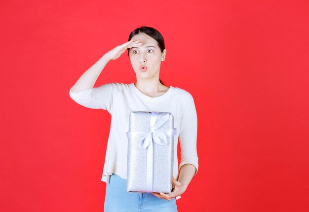 Bella dama sorprendida sosteniendo caja de regalo y mirando a otro lado