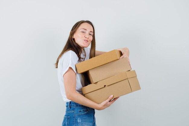 Bella dama sosteniendo cajas en blusa blanca y mirando alegre, vista frontal.