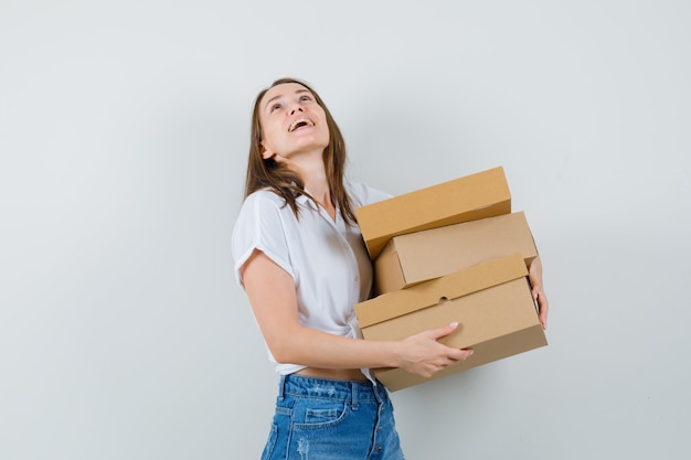 Bella dama sosteniendo cajas mientras mira hacia arriba en la vista frontal de la blusa blanca.