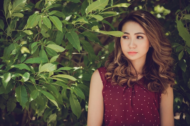 Una bella modelo asiática posando en medio de las hojas del árbol en el parque