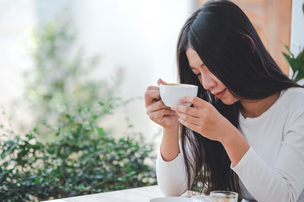 Una bella mujer con una camisa blanca de manga larga sentada en una cafetería.