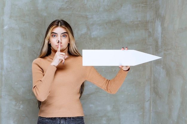 Foto gratuita bella mujer con una flecha haciendo señal silenciosa sobre una piedra