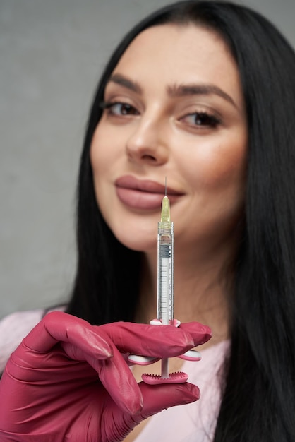 Bella mujer con guantes rosados mostrando una jeringa llena a la cámara retrato en primer plano de