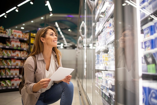 Bella mujer con lista de compras comprando alimentos en el supermercado