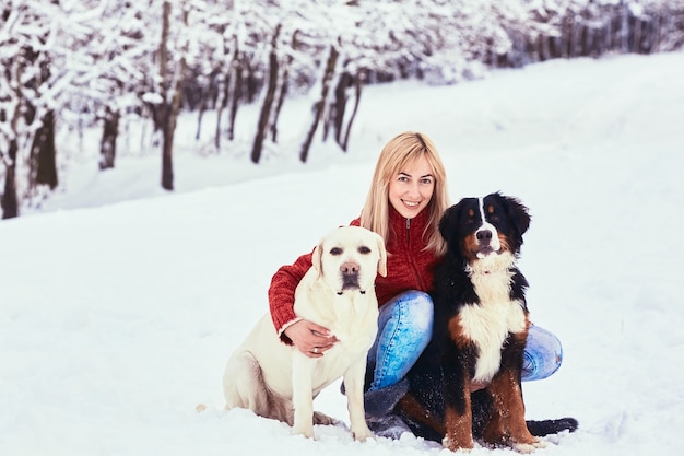 La bella mujer con perro sentado en la nieve
