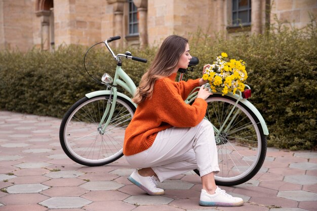 Bella mujer posando junto a la bicicleta con flores al aire libre