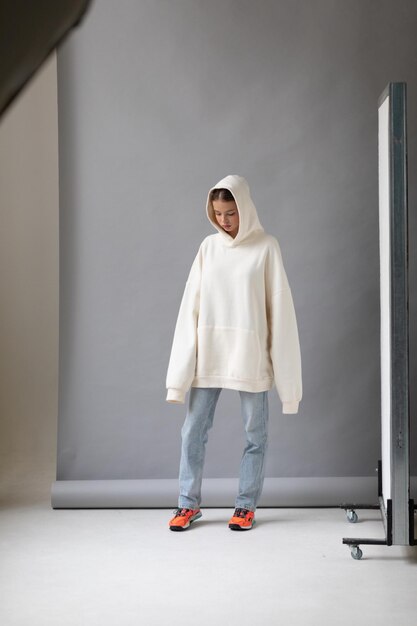 Bella mujer rubia con una sudadera blanca y vaqueros azules posando sobre un fondo gris