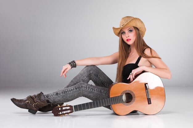 La bella mujer con sombrero de vaquero y guitarra acústica.