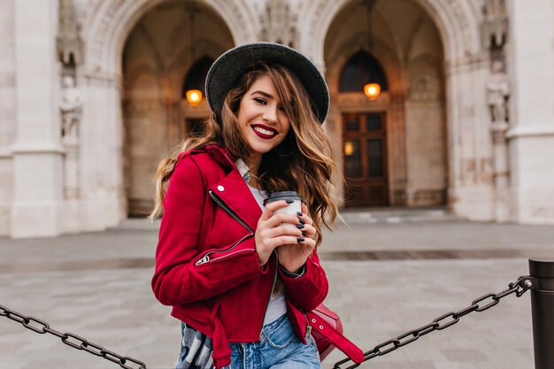 Bella mujer sonriendo a la cámara mientras bebe café con leche junto al museo