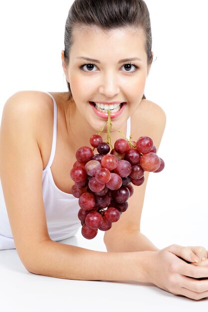 Bella mujer sosteniendo un racimo de uvas por sus dientes