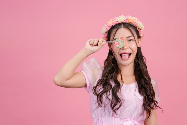 Una bella mujer vestida con una princesa rosa está jugando con su dulce caramelo en un rosa.