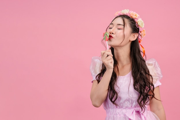 Una bella mujer vestida con una princesa rosa está jugando con su dulce caramelo en un rosa.