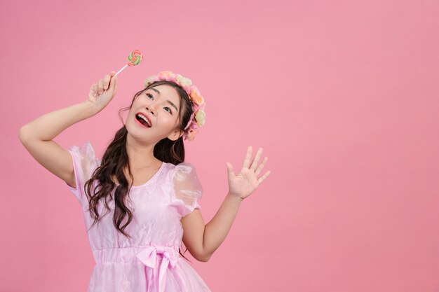 Una bella mujer vestida con una princesa rosa está jugando con su dulce caramelo en un rosa.