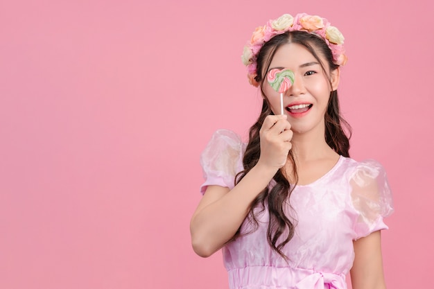 Una bella mujer vestida con una princesa rosa está jugando con su dulce caramelo en un rosa.