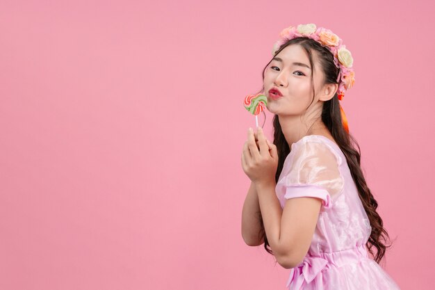 Una bella mujer vestida con una princesa rosa está jugando con su dulce caramelo en un rosa.